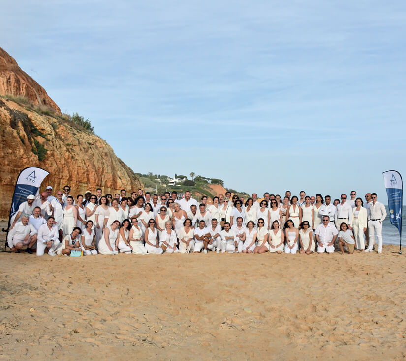 Photo de groupe des agents AXO sur une plage à Faro avec en premier plan du sable et au dessus du groupe le ciel bleu du Portugal.